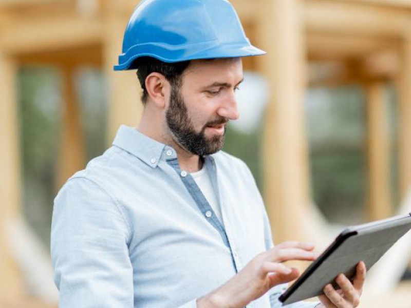 Homme tenant sa tablette numérique devant sa maison en cours de construction