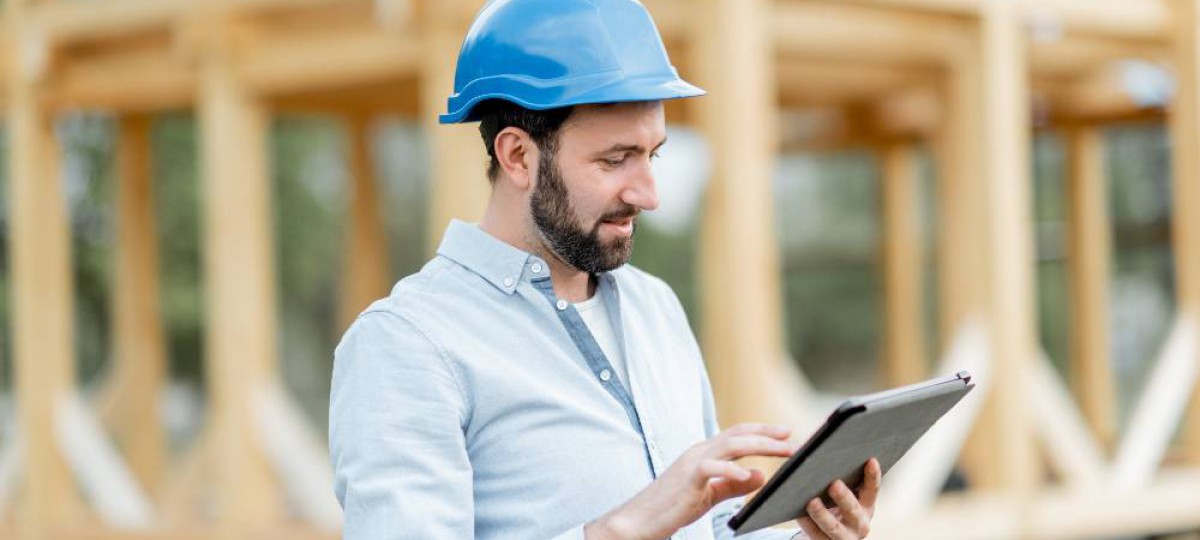 Homme tenant sa tablette numérique devant sa maison en cours de construction