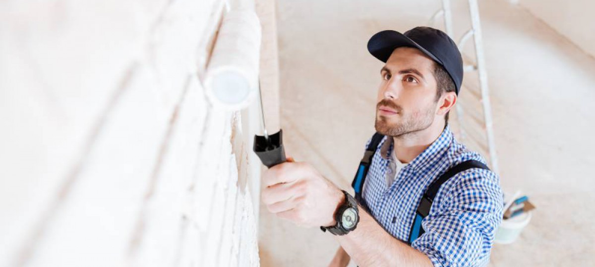 Homme peignant un mur en blanc après la pose d'une isolation et d'un revêtement décoratif