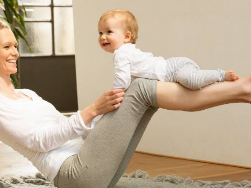 mère assise en équilibre au sol avec son bébé sur les jambes