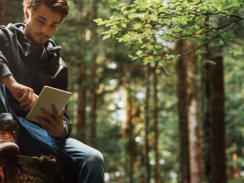 Un jeune homme est assit dans une forêt et consulte des informations sur la finance responsable