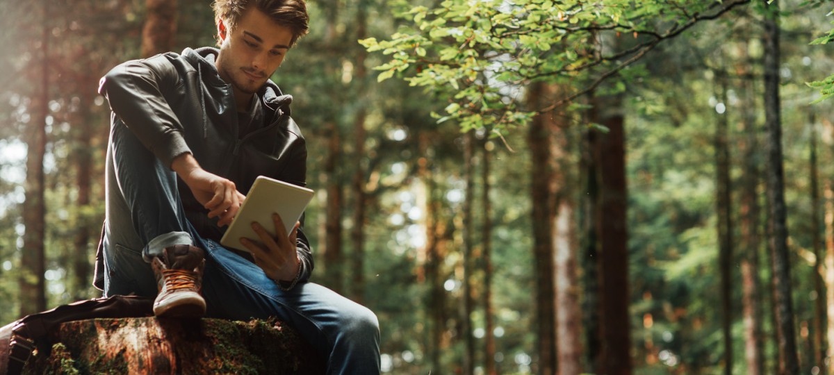 Un jeune homme est assit dans une forêt et consulte des informations sur la finance responsable