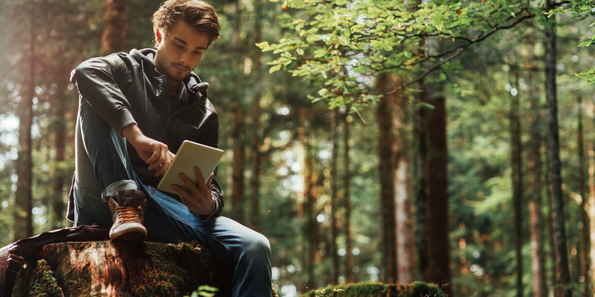 Un jeune homme est assit dans une forêt et consulte des informations sur la finance responsable