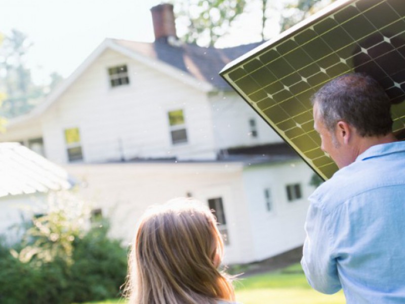 Homme portant un panneau solaire à installer sur sa maison, une petite fille l'accompagne