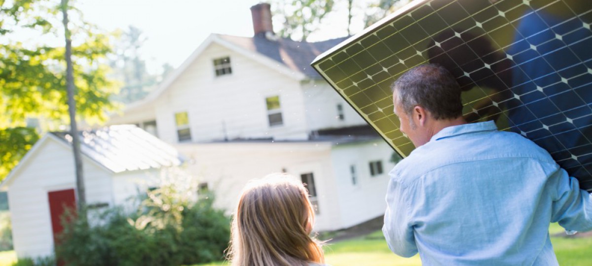 Homme portant un panneau solaire à installer sur sa maison, une petite fille l'accompagne