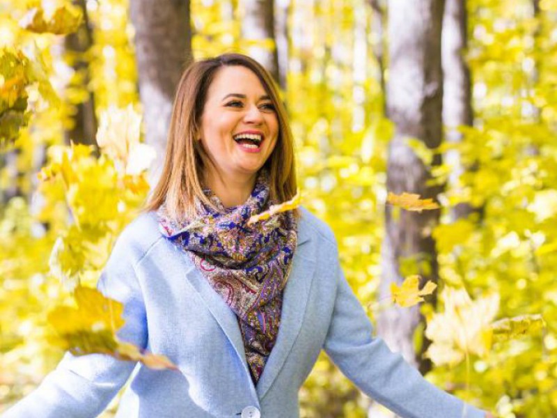 femme souriante laçant des feuilles dans un bois en automne