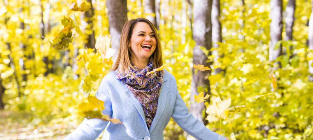 femme souriante laçant des feuilles dans un bois en automne